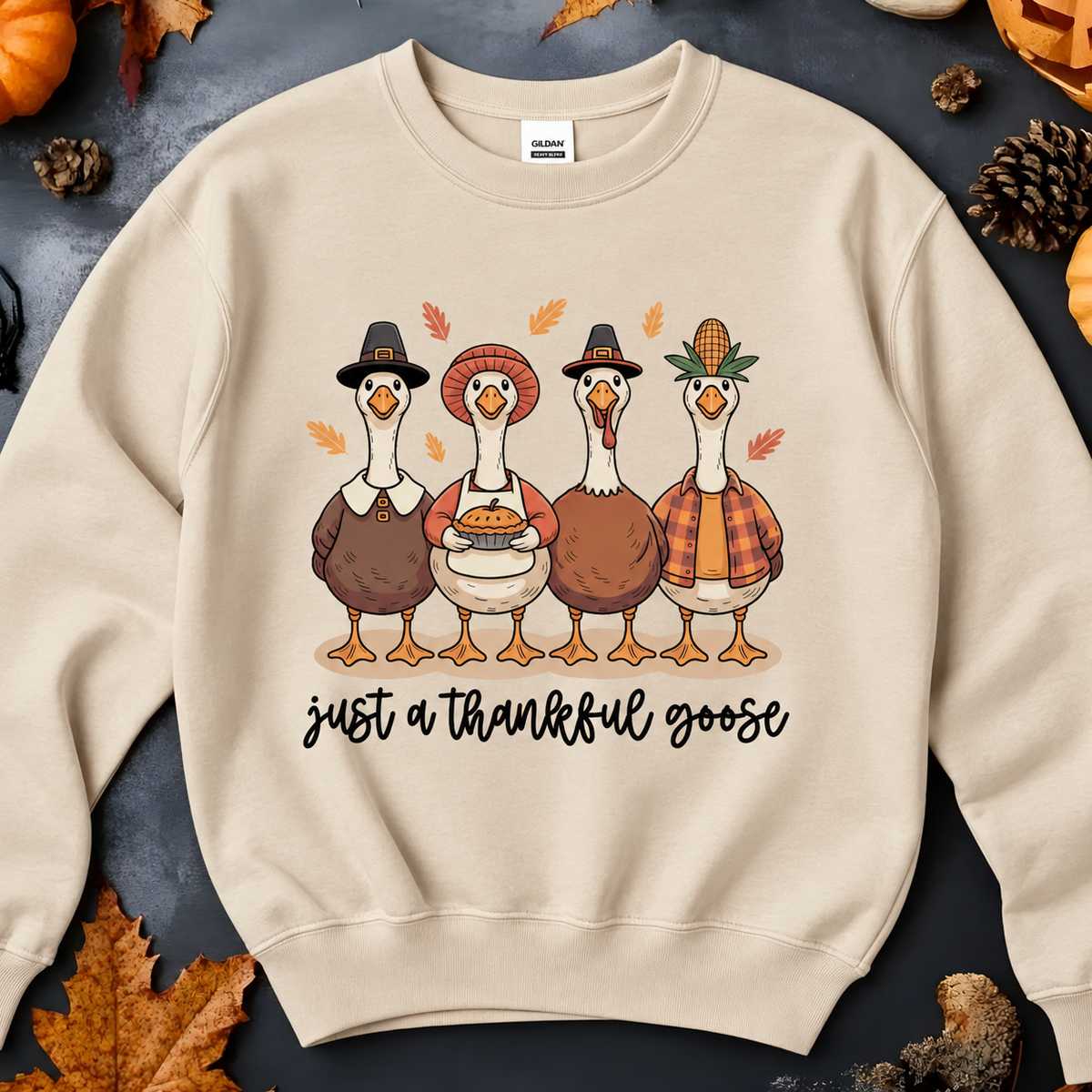 A sand crewneck sweatshirt featuring a graphic of four cartoon turkeys dressed as Pilgrims with the text 'just a thankful goose' underneath.