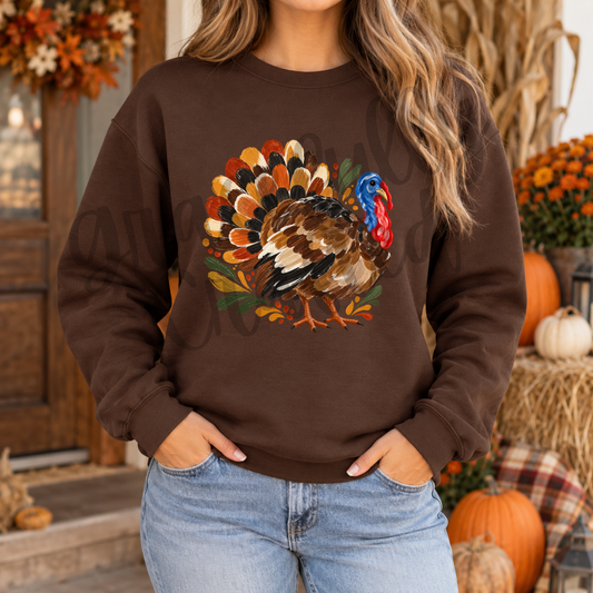 A woman wearing a brown crewneck sweatshirt with a large colorful turkey graphic on the front.