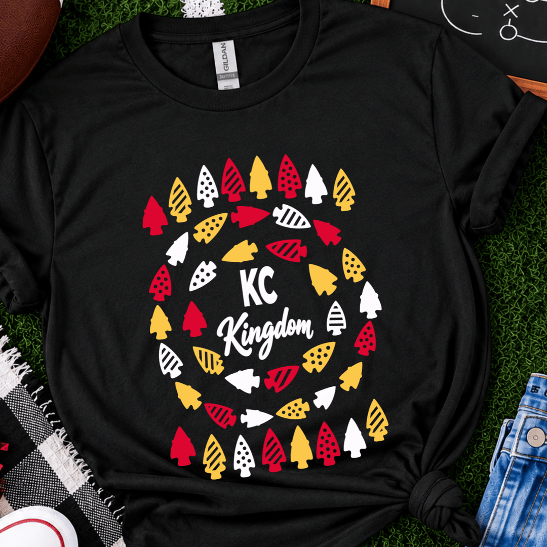 Kansas City Chiefs design featuring red, gold, and white arrowheads with playful polka dot and striped patterns arranged around the words “KC Kingdom” in white lettering on a black shirt.