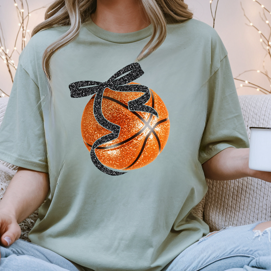 Sage green shirt featuring an orange basketball with a black bow tied around the top.