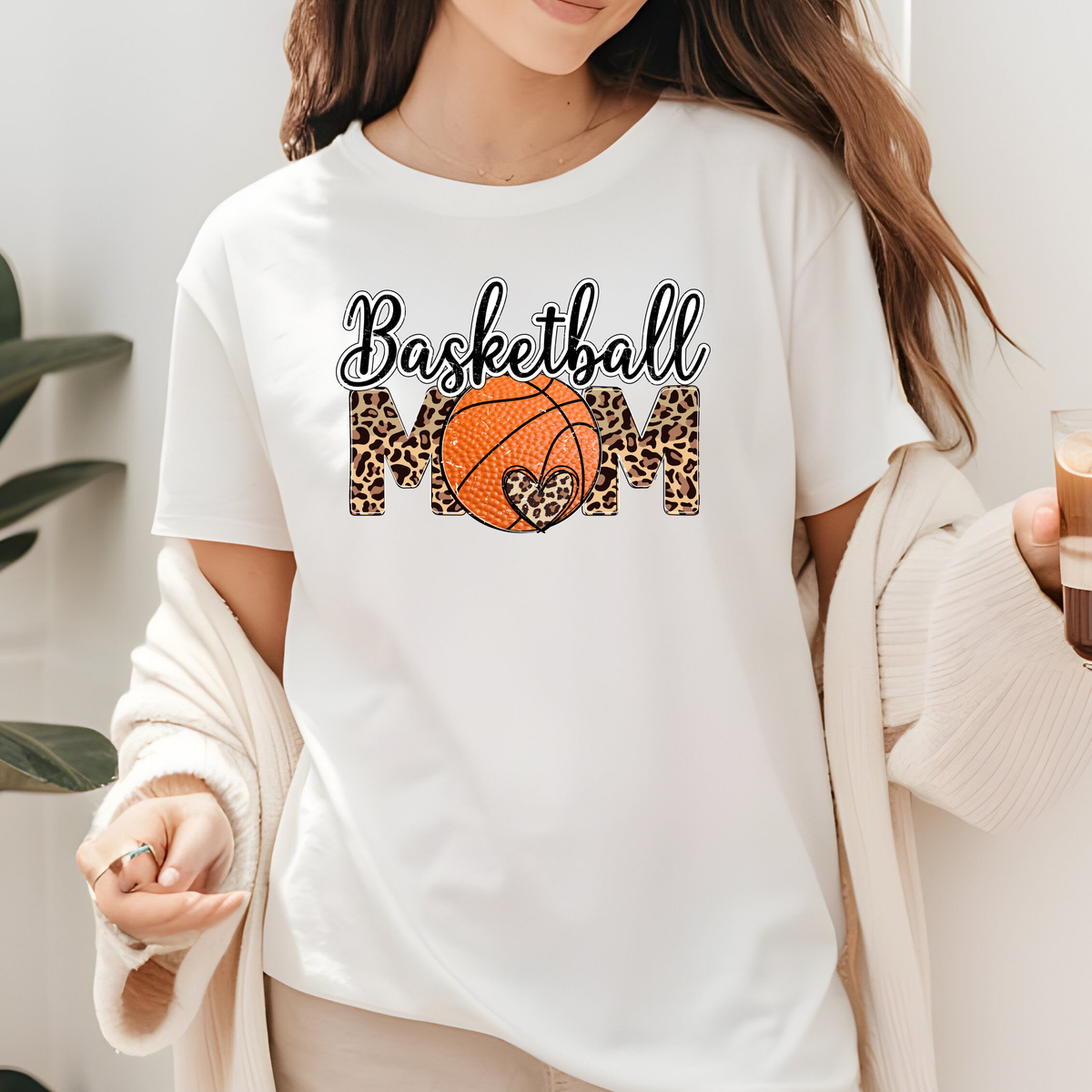 White shirt featuring Basketball Mom lettering with an orange basketball and decorative bow accents.