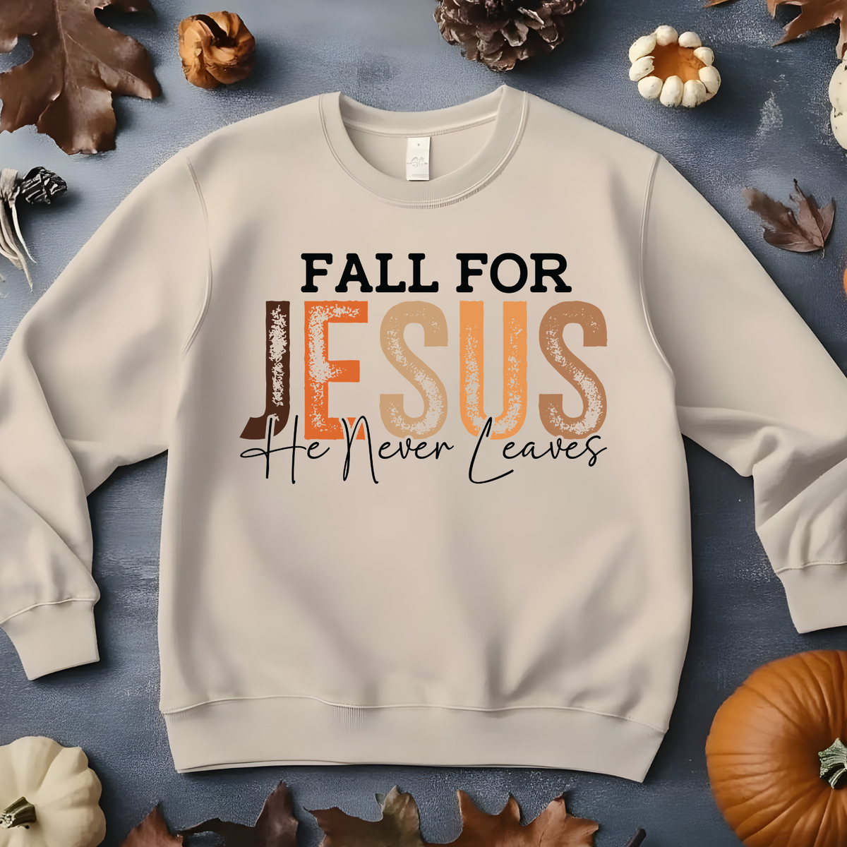 Sand colored crewneck sweatshirt with a graphic reading 'FALL FOR JESUS He Never Leaves' in black and orange text