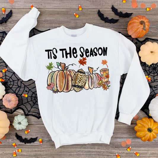 A white crewneck sweatshirt features a graphic of autumn pumpkins and the text 'IT'S THE SEASON' in black.