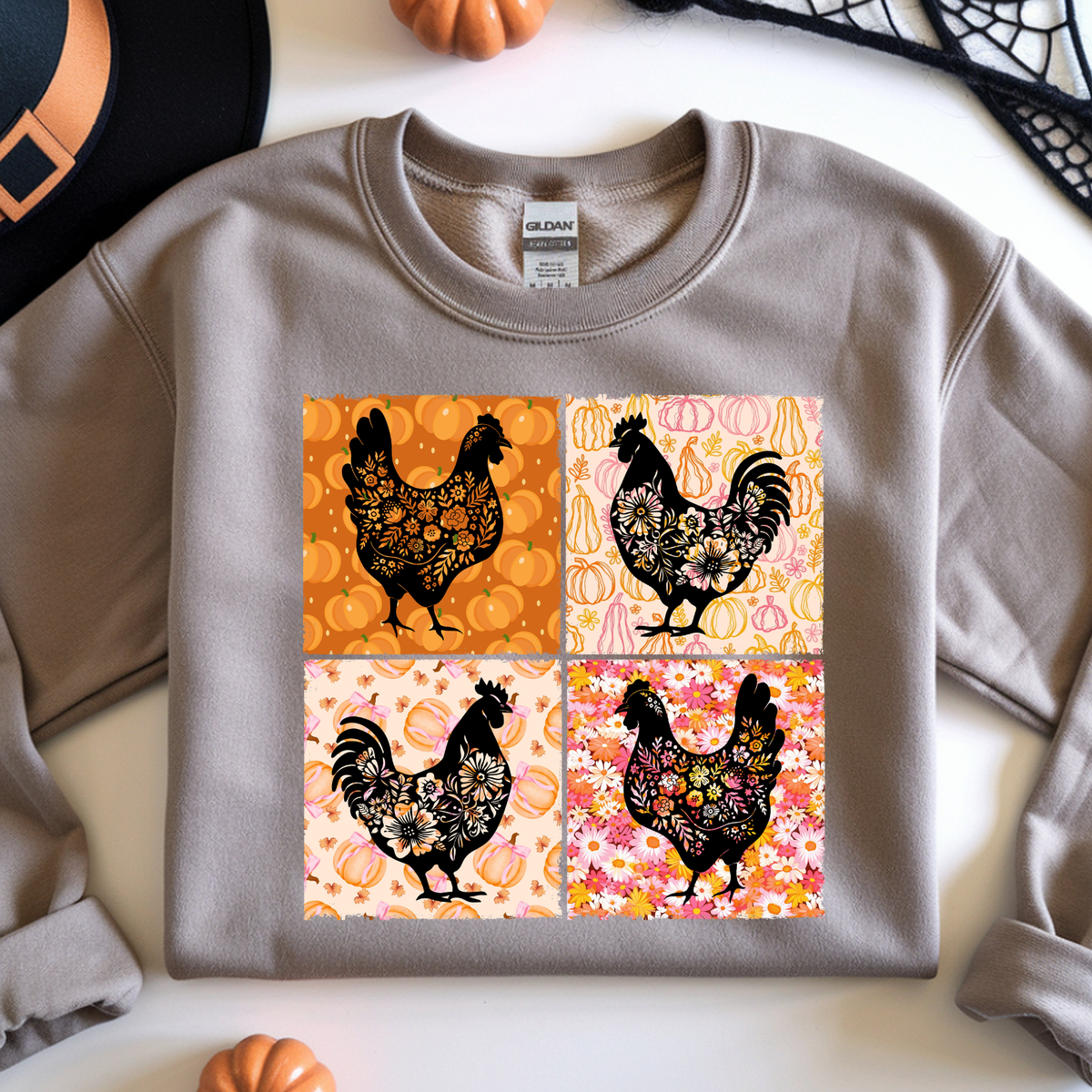 A sand crewneck sweatshirt featuring a four-panel graphic print of black rooster silhouettes decorated with intricate floral and geometric patterns on orange, pink, and cream backgrounds.