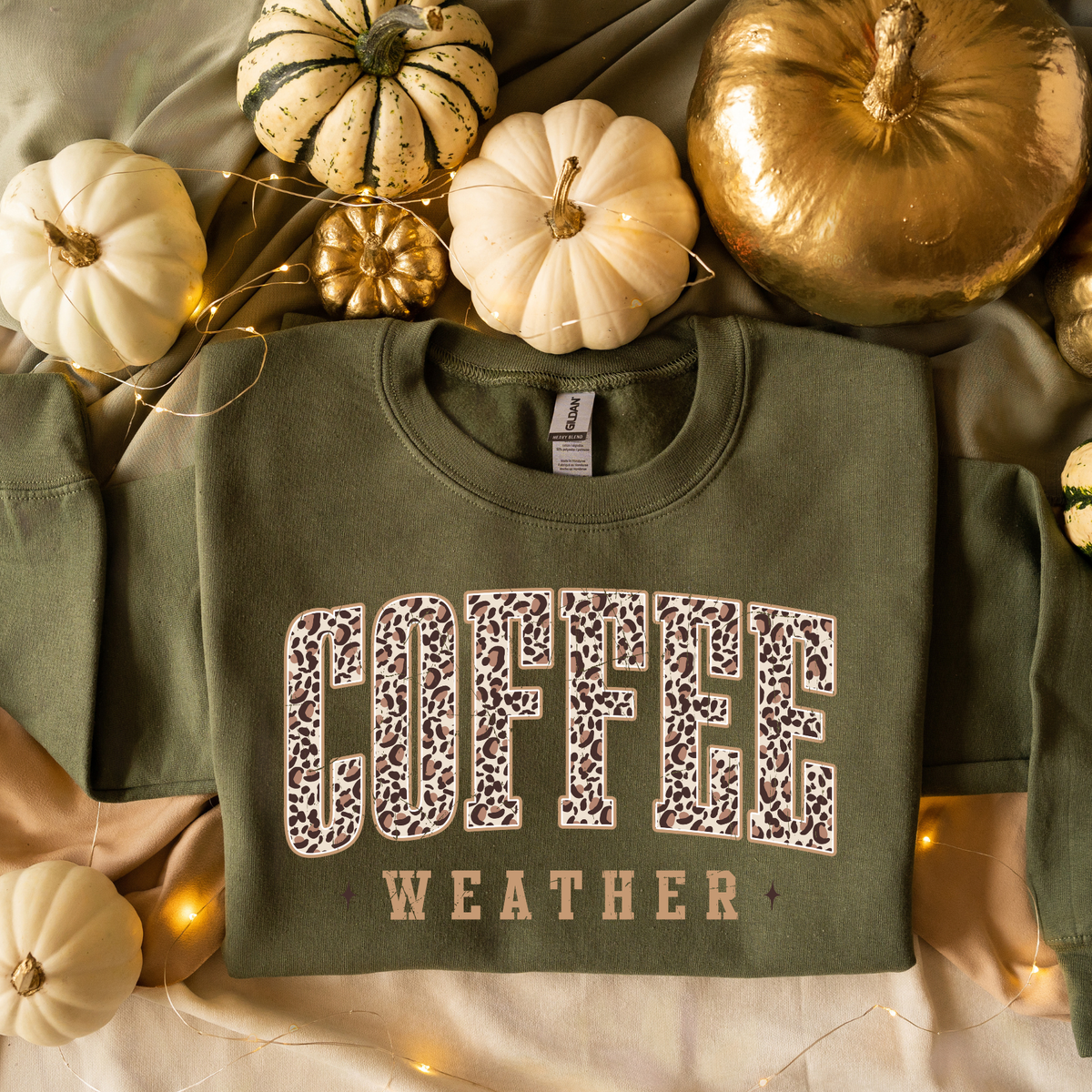 A military green crewneck sweatshirt with 'COFFEE WEATHER' printed on the front in leopard-print and tan lettering