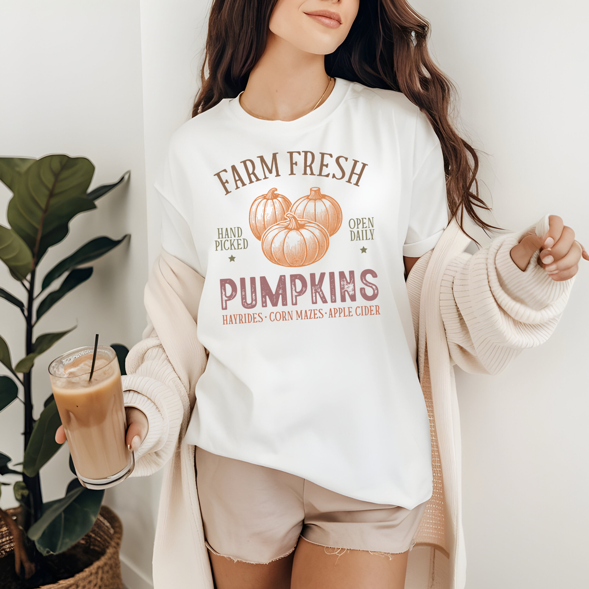 A woman wearing a white graphic t-shirt with a 'Farm Fresh Pumpkins' design in muted orange-brown tones