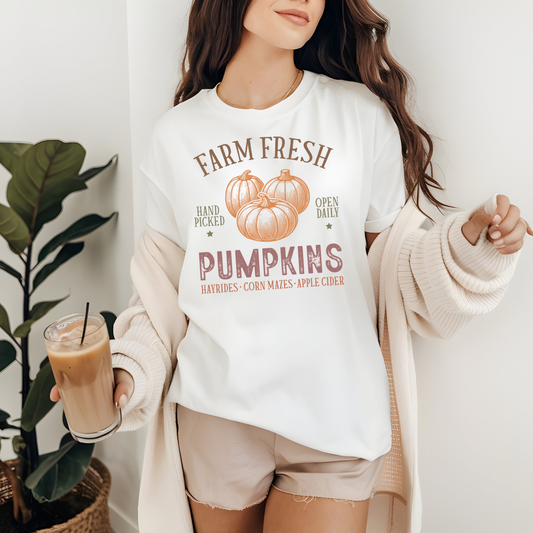 A woman wearing a white graphic t-shirt with a 'Farm Fresh Pumpkins' design in muted orange-brown tones
