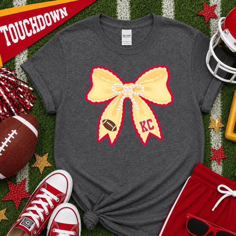 Dark heather gray t-shirt featuring a large yellow bow with red trim, pearl accents, a football, and red KC lettering, inspired by Kansas City Chiefs football.