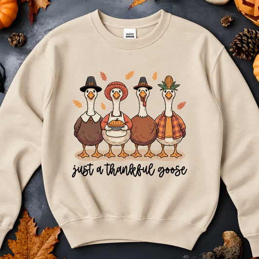A sand crewneck sweatshirt featuring a graphic of four cartoon turkeys dressed as Pilgrims with the text 'just a thankful goose' underneath. 
